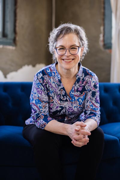 woman with glasses sitting on a blue couch, leaning slightly forward